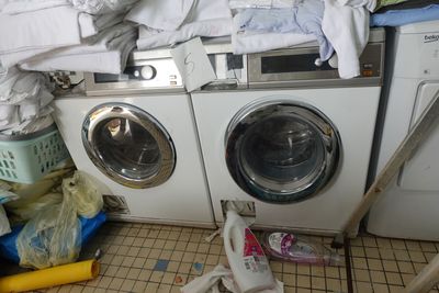 une machine à laver et un sèche-linge dans une pièce où il y a beaucoup de vêtements par terre