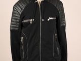La veste est noire et comporte des fermetures éclair sur les manches.