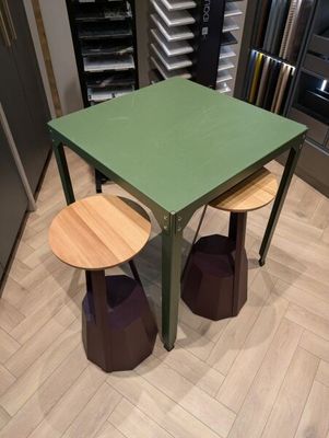 une table verte et deux tabourets dans une pièce