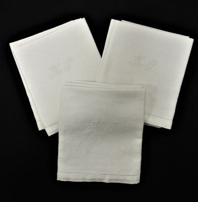 trois serviettes blanches ornées de monogrammes brodés sur fond noir