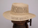 chapeau de paille beige posé sur un support en bois, sur fond gris
