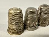 three silver thimbles are lined up on a white surface