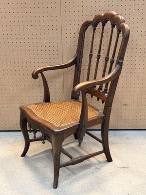Une vieille chaise en bois avec une assise tressée est posée devant un mur.