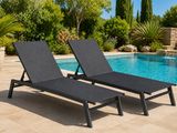 two black lounge chairs next to a swimming pool with trees in the background