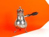 une théière en argent avec une anse noire sur fond orange