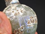 a hand holding a small vase with a stone decoration on it