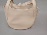 sac à main en cuir beige sur fond gris, muni d'une bandoulière et d'une poignée