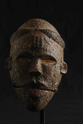un gros plan d'un masque en bois posé sur un socle, sur fond noir