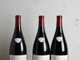 trois bouteilles de vin sont posées sur une table en bois devant un mur