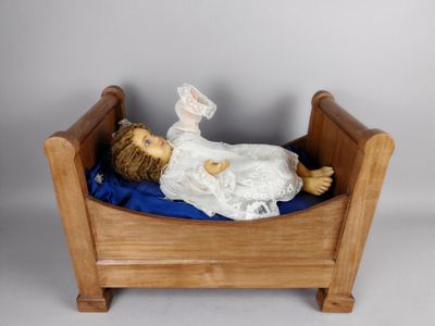 une poupée allongée dans un lit en bois, recouverte d'une couverture bleue
