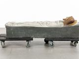 a sculpture of a person laying in a bed on wheels