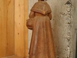 a wooden statue of a woman holding a basket on a shelf