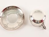 a silver cup and saucer on a white surface