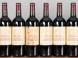 six bottles of red wine lined up on a wooden shelf