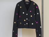 une veste noire avec des boutons multicolores, suspendue à un cintre