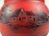 a red vase with a picture of a house on it