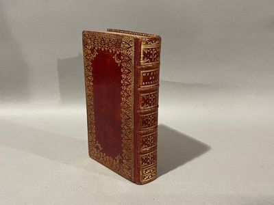 un livre rouge aux bords dorés posé sur une surface blanche