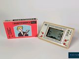 a small electronic game in a box next to it ' s box