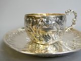 a silver cup and saucer sitting on a silver plate