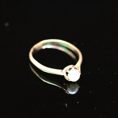 un gros plan d'une bague en or sertie d'une perle sur un fond noir