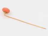 a gold stick pin with a coral colored bead on a white background