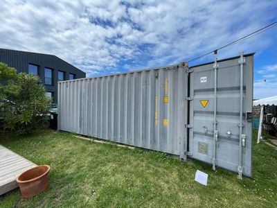 un conteneur maritime dans une cour, avec une terrasse en bois et une plante en pot au premier plan