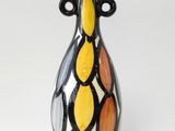 un vase noir et jaune posé sur une surface blanche