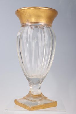 a glass vase with a gold top on a white pedestal
