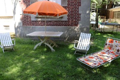 Des chaises et un parasol sont posés dans l'herbe devant une maison