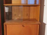 a tall wooden bookcase with a glass door in the corner of the room