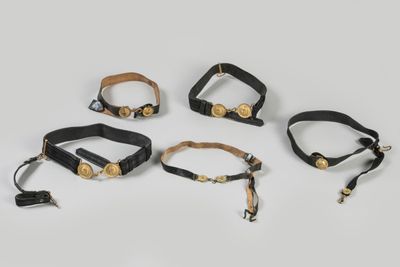 a set of five black leather wrist cuffs with brass hardware