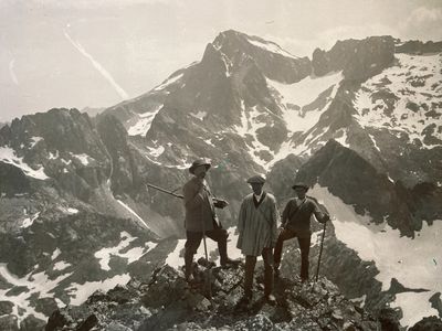 three men standing on top of a mountain with skis