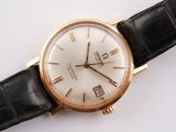 a gold wrist watch with a white dial on a black strap