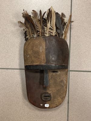 un masque accroché au mur, orné de plumes