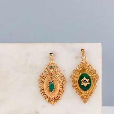 une paire de boucles d'oreilles vertes et dorées posées sur une surface en marbre