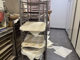 several trays of pizza sit on a rolling cart in a kitchen