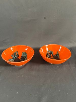 une paire de bols orange décorés d'animaux, posés sur une table