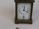une petite horloge et une clé posées sur une surface blanche