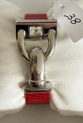 a silver watch on a red strap with a tag attached to it