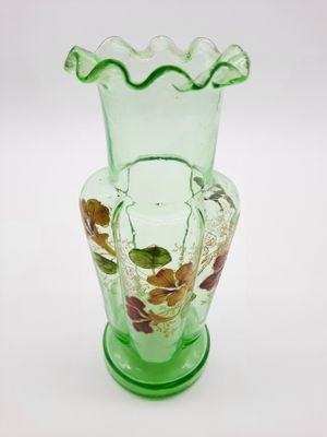 un vase en verre vert orné de feuilles, posé sur une surface blanche