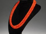 an orange beaded necklace on a black mannequin stand