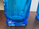 three blue glass vases sitting on a wooden table with a white wall in the background