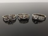three diamond engagement rings on a black surface