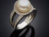 a white pearl and diamond ring on a black surface