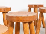 several wooden stools are lined up in a row against a white wall