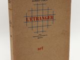 un livre marron avec des lettres rouges, posé sur une surface blanche