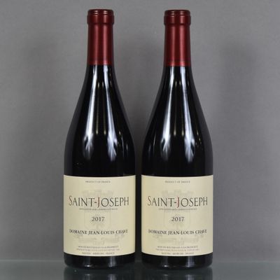 Deux bouteilles de vin sont posées sur une table en verre devant un mur gris.