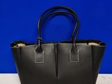 un sac fourre-tout en cuir noir posé sur une table blanche, sur fond bleu