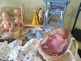 many baby dolls sitting on a bed next to a wicker chair