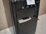 a small black refrigerator sitting on the sidewalk next to a wall